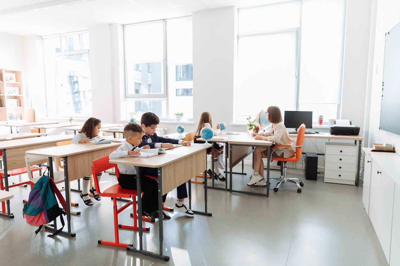 Elementary students studying together in a bright classroom with a teacher assisting.